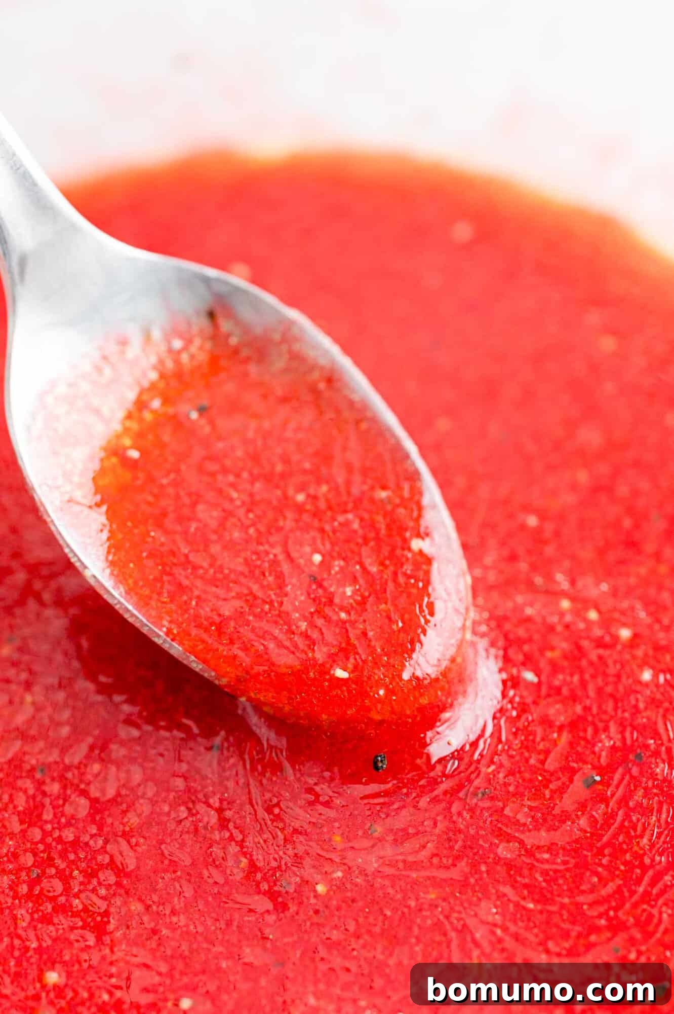 A spoon holds a generous amount of freshly made raspberry vinaigrette dressing, showing its smooth texture and rich color.