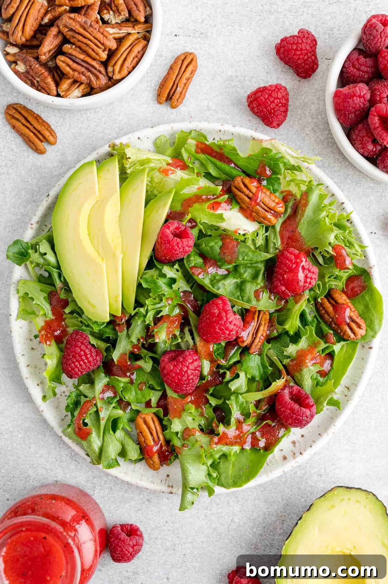 A vibrant salad featuring raspberry vinaigrette, fresh raspberries, pecans, and creamy avocado, showcasing a perfect balance of flavors and textures.