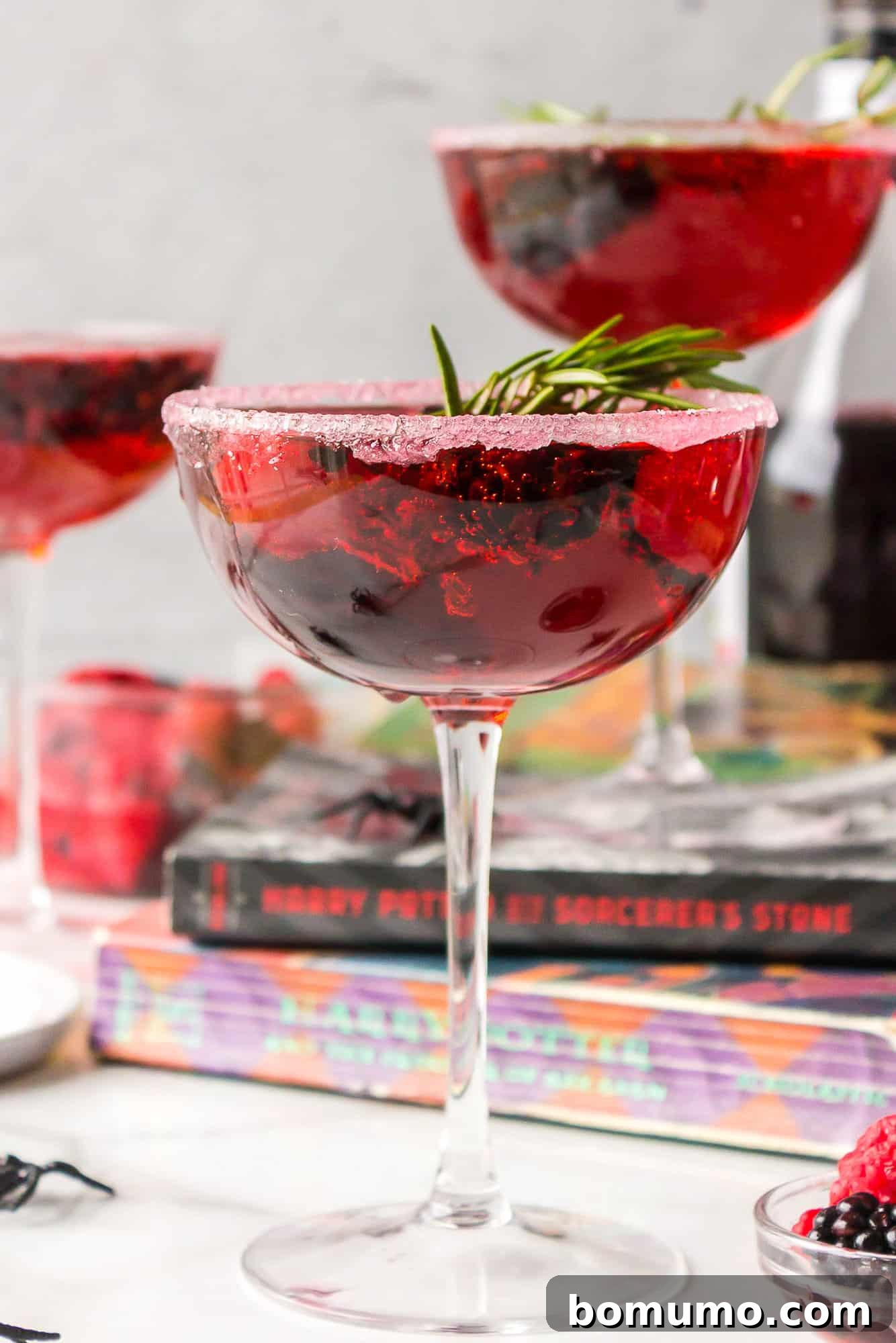 A vibrant berry-red Love Potion Cocktail, garnished beautifully, with classic books in the background, suggesting an enchanting blend of mixology and storytelling.