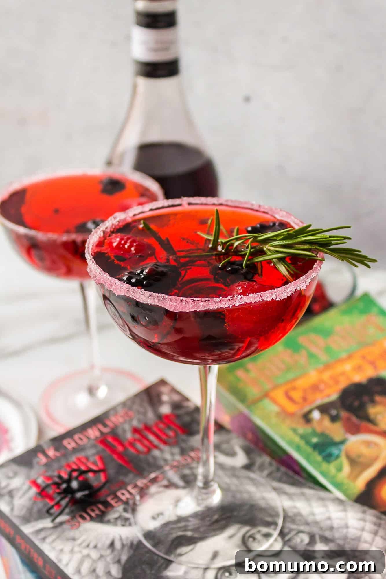 Two perfectly prepared Love Potion Cocktails, glowing with a bright red hue, adorned with fresh fruit and aromatic rosemary garnishes, set against a stylish backdrop.