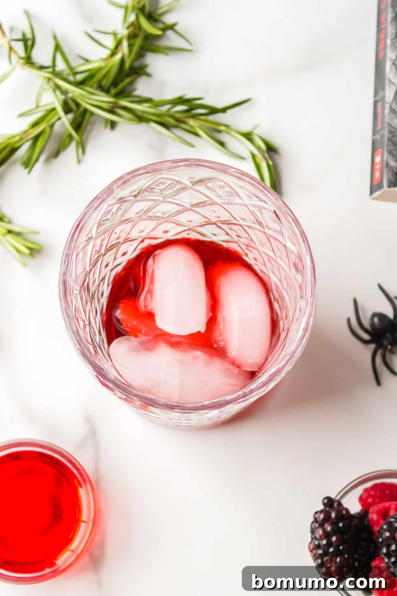 The vibrant red cocktail ingredients, including raspberry liqueur, vodka, and grenadine, are meticulously poured over ice into a cocktail shaker, ready for mixing to create the Love Potion Cocktail.