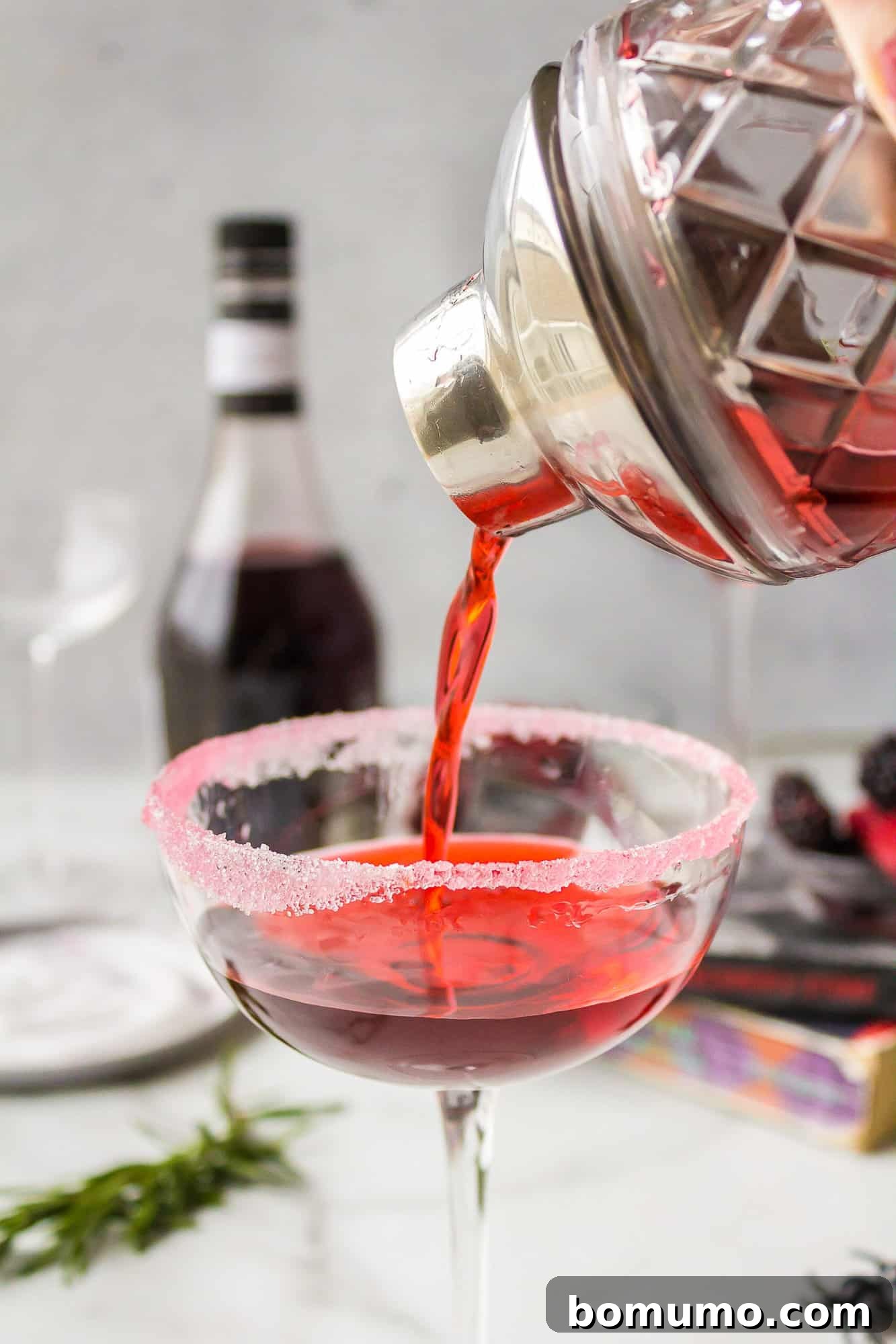 The crimson Love Potion Cocktail is elegantly poured from a shaker into a delicate coupe glass, showcasing its rich color and inviting texture, just before garnishing.