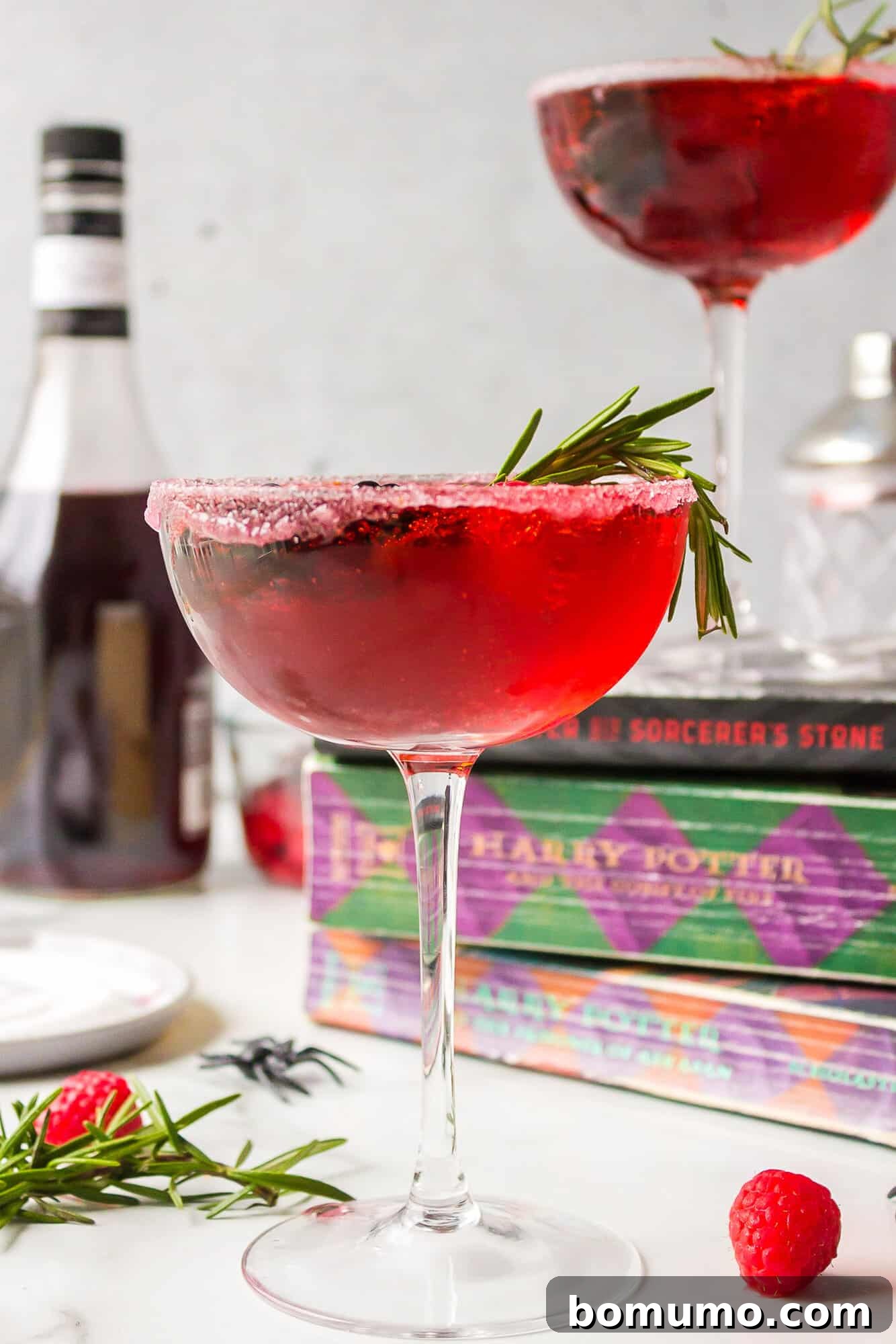 A beautifully presented Love Potion Cocktail, glowing red, artfully placed amongst a stack of classic Harry Potter books, blending mixology with a touch of literary magic.