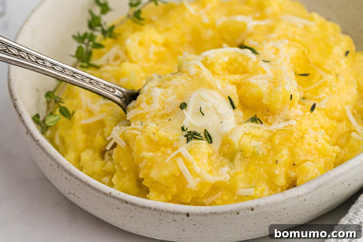 Close-up of creamy polenta in a bowl, garnished with fresh herbs and a pat of butter, showcasing its inviting texture.