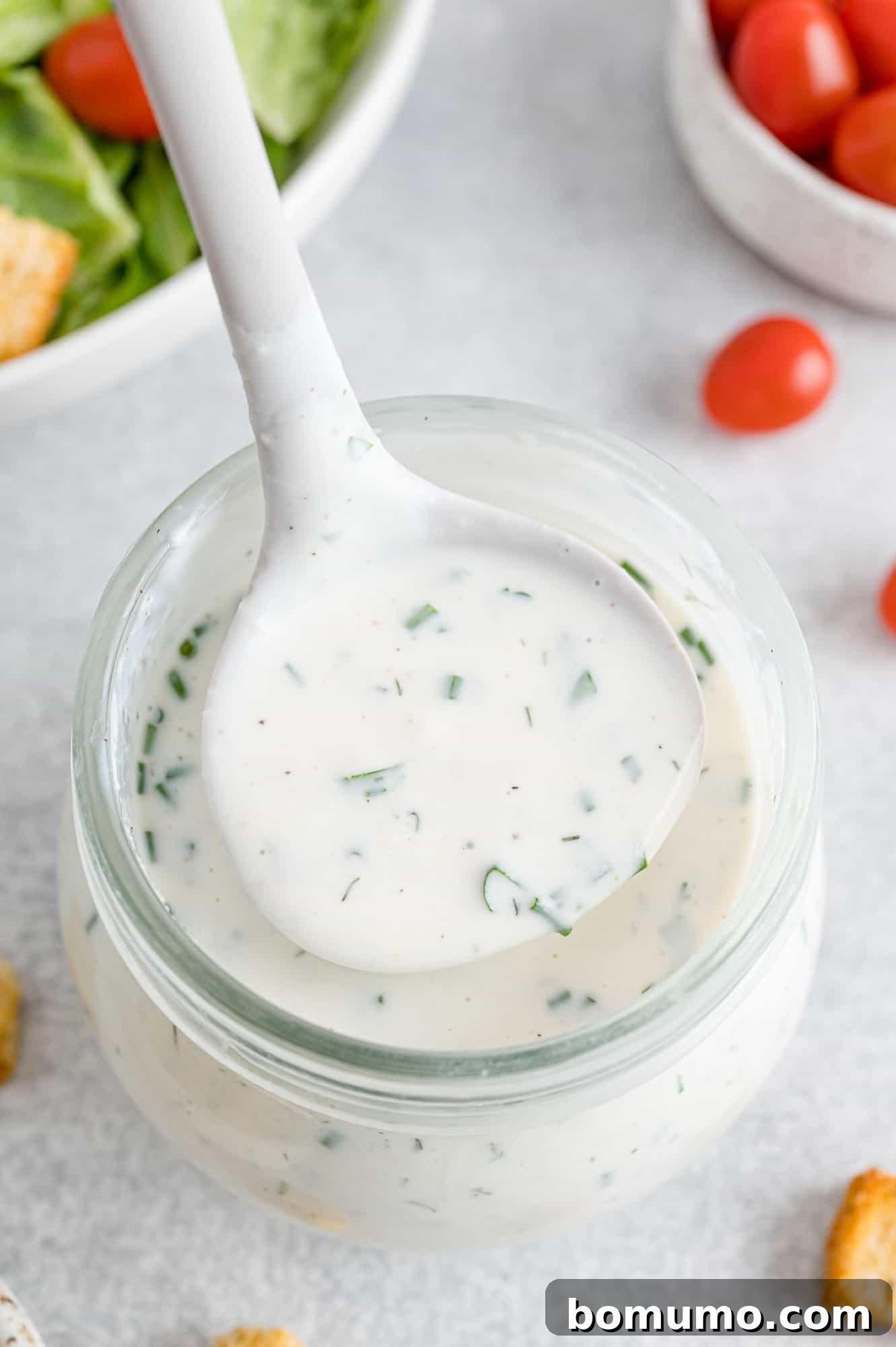 A ladle filled with homemade healthy ranch dressing, carefully held over a glass jar, highlighting its creamy texture.