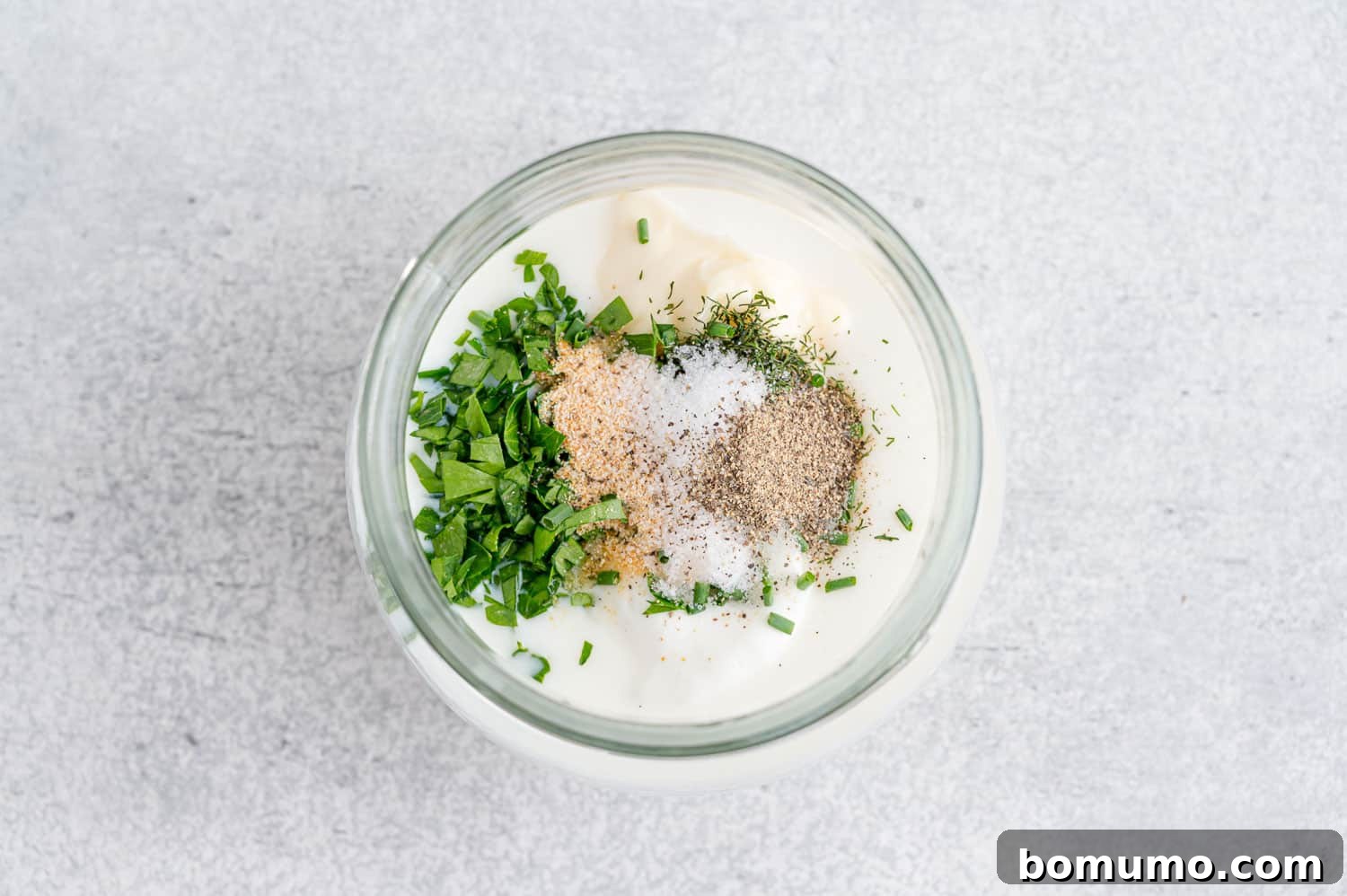 All the unmixed ingredients for healthy ranch dressing neatly arranged inside a glass jar, ready for shaking.