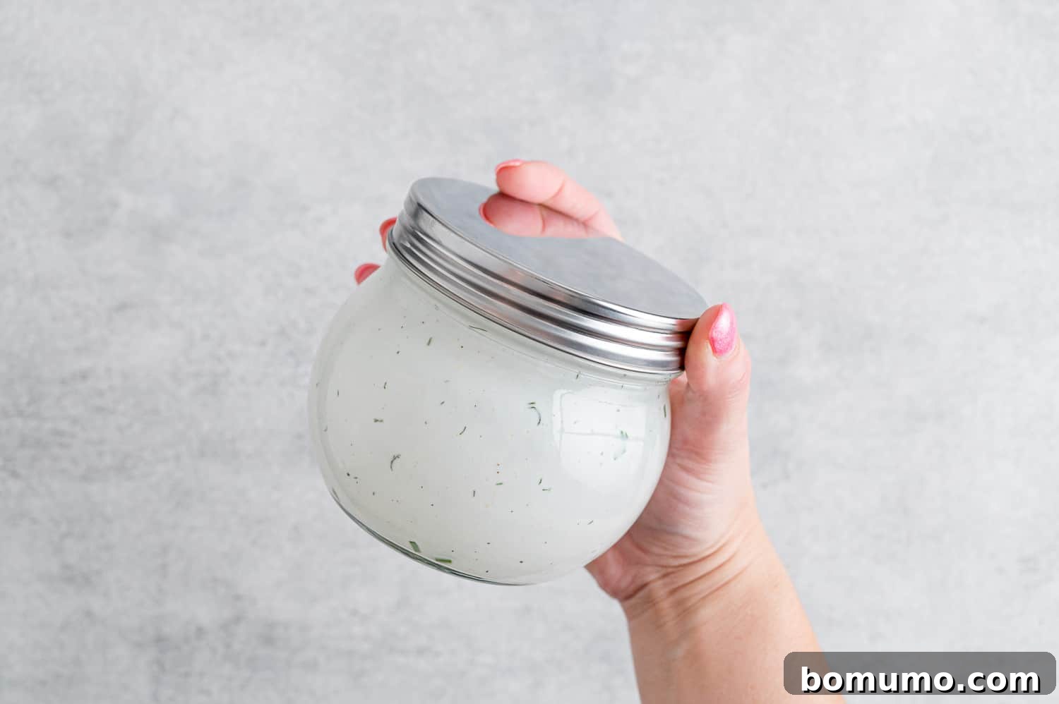 A glass jar of homemade ranch dressing being vigorously shaken, illustrating the mixing process.