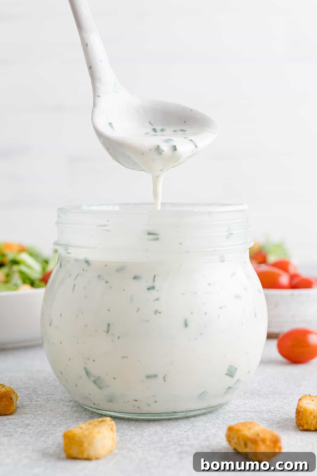 Healthy ranch dressing being poured from a ladle back into a jar, demonstrating its smooth and perfectly pourable consistency.