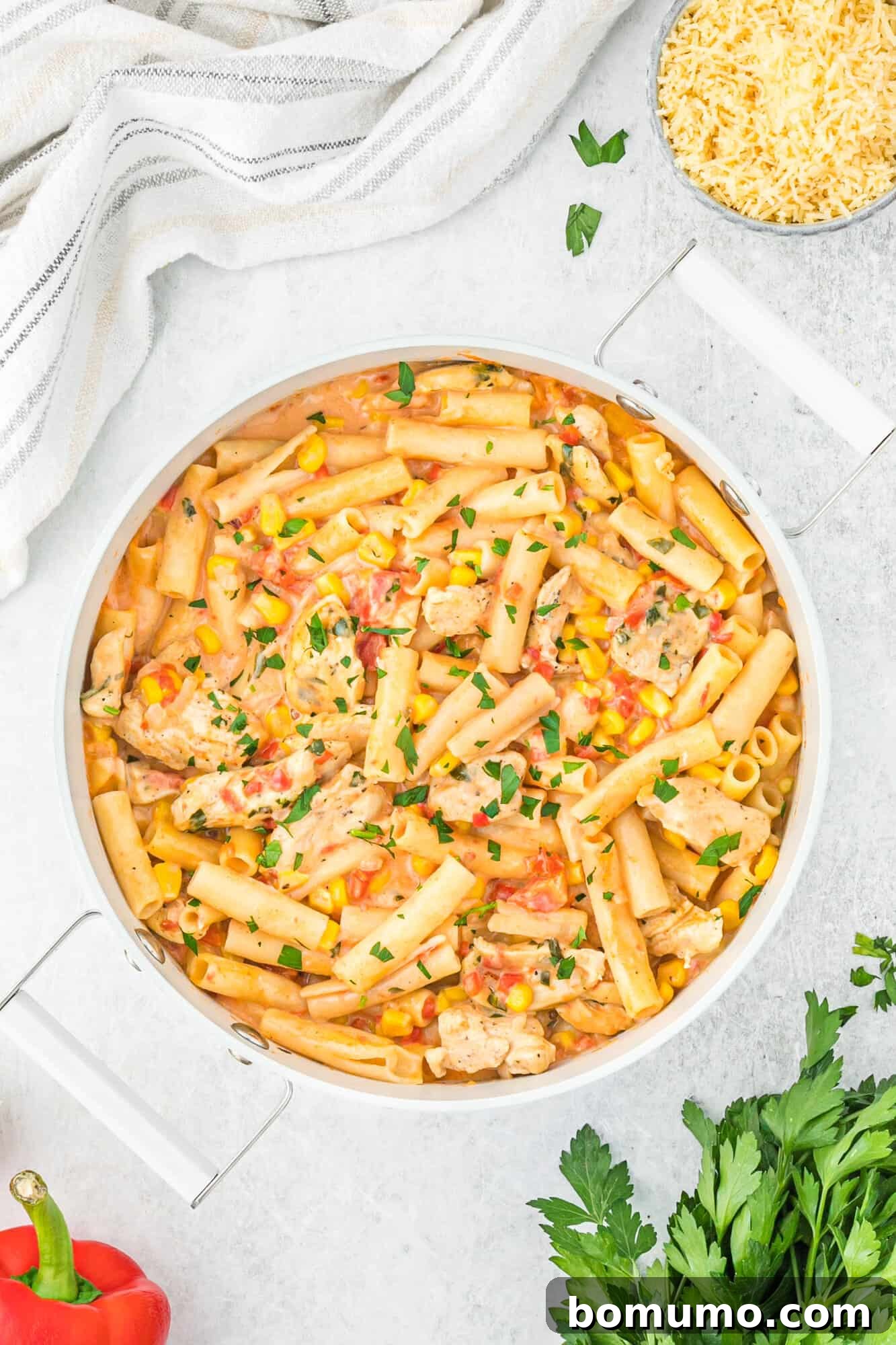 Overhead view of a bowl of Cajun chicken pasta surrounded by fresh ingredients and spices.