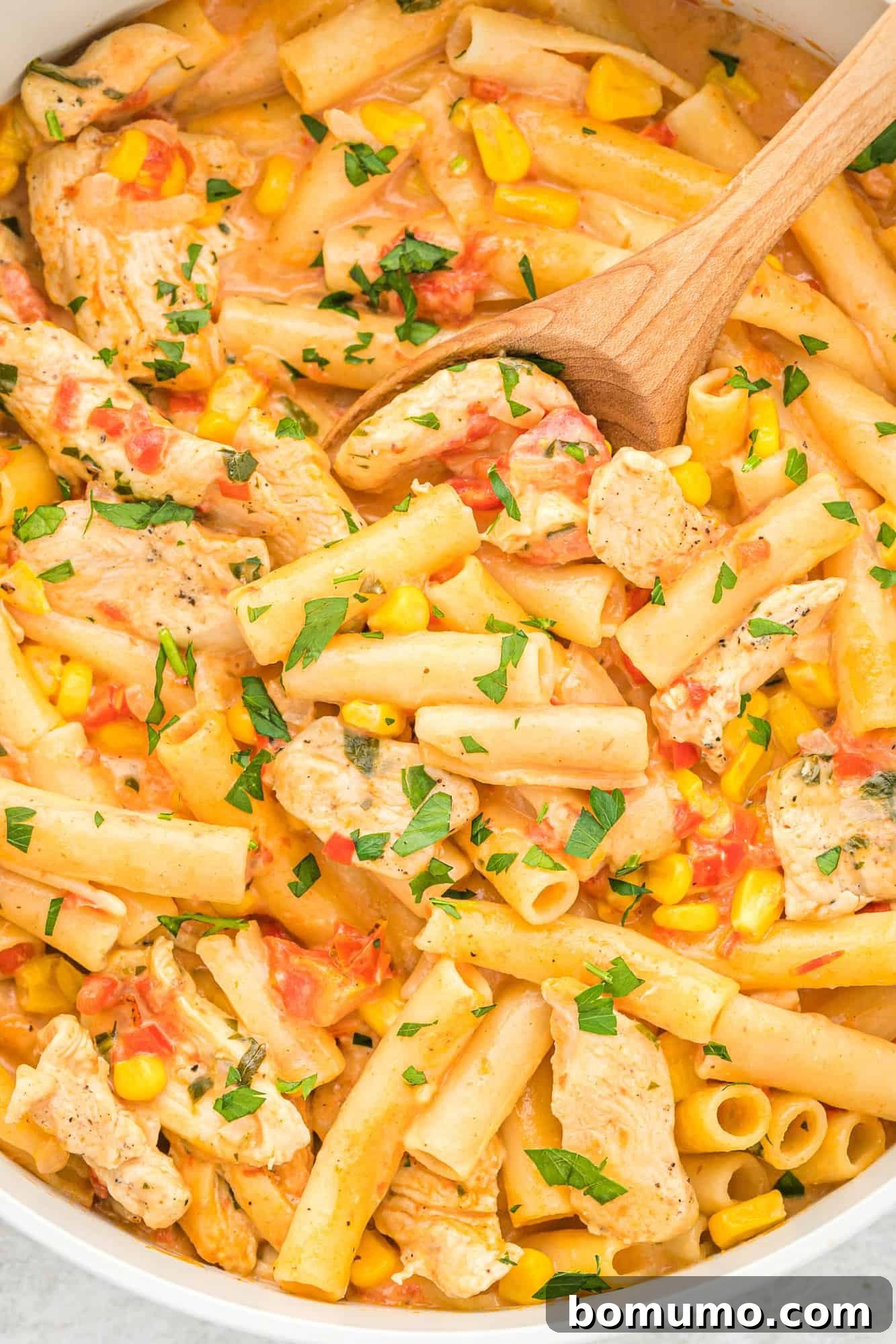 Cajun chicken pasta freshly made in a large pan with a wooden serving spoon.