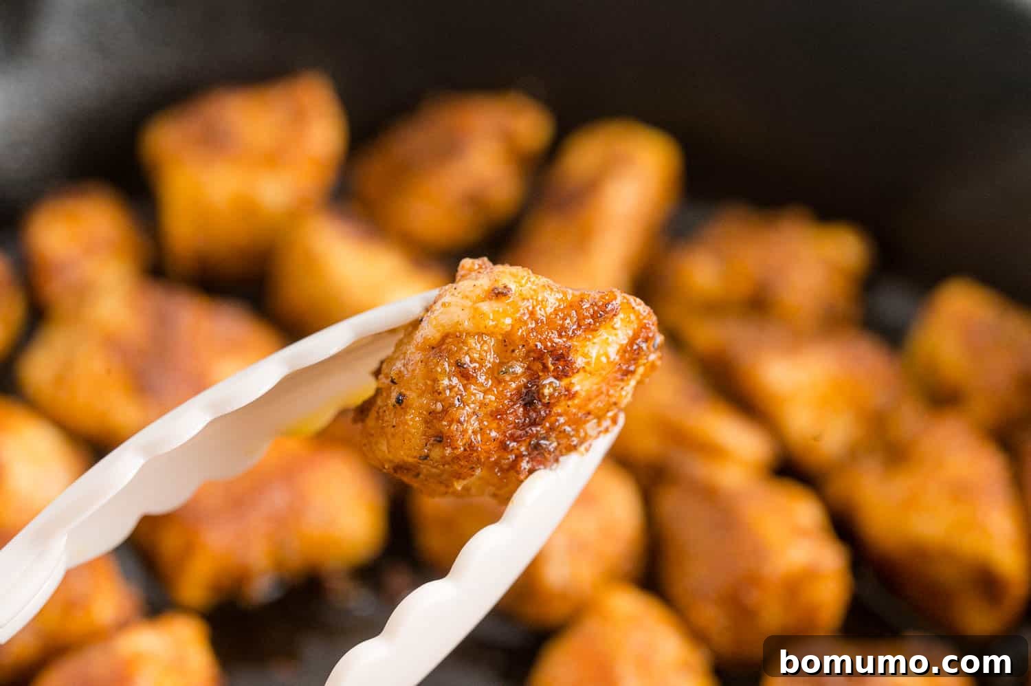 Golden Chicken Bites 8 Close-up of crispy, golden-brown chicken bites being lifted from a skillet with kitchen tongs, ready for serving.