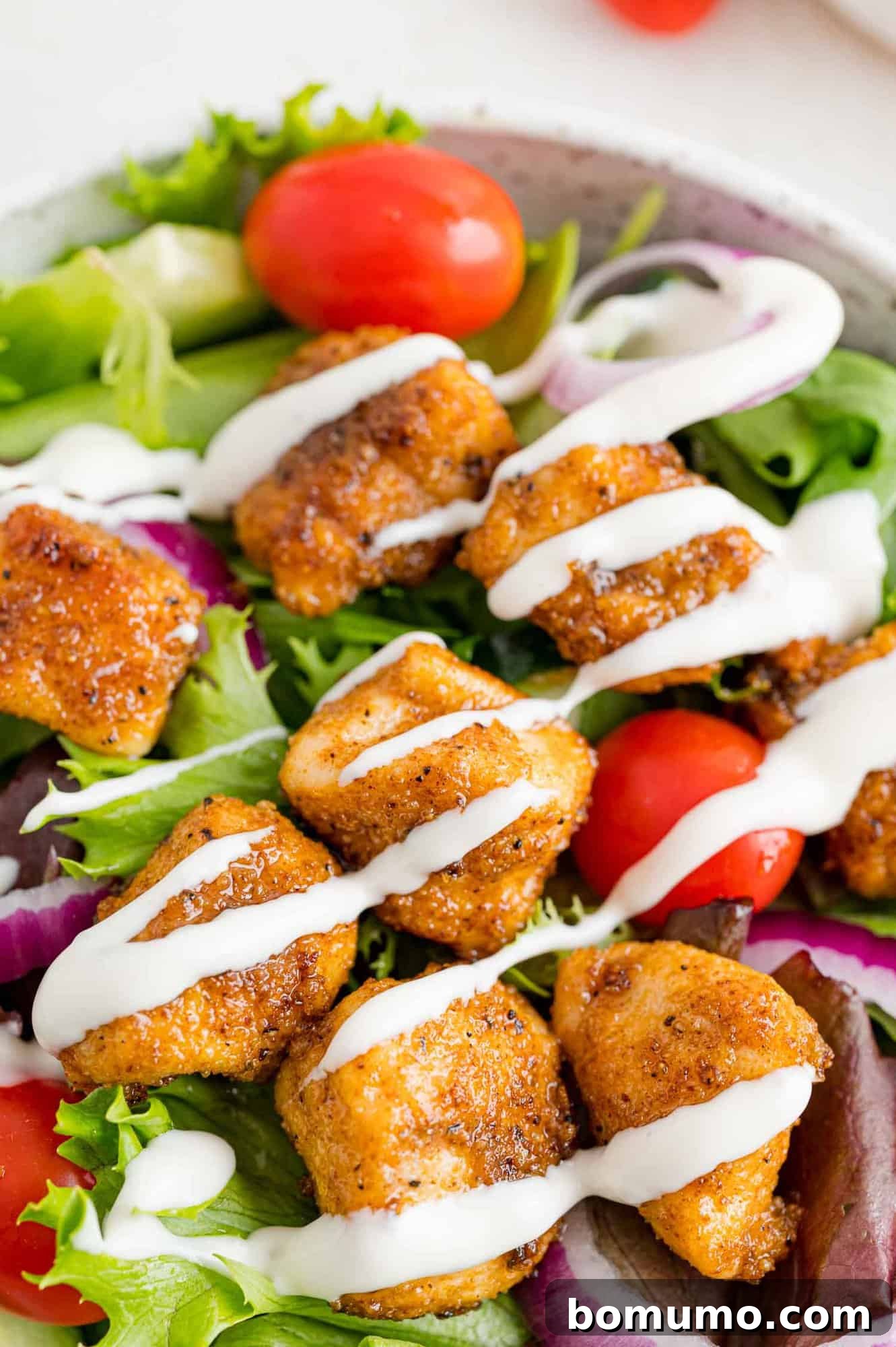 Golden Chicken Bites 10 A vibrant salad topped with an abundance of golden, crispy chicken bites and drizzled generously with creamy ranch dressing.