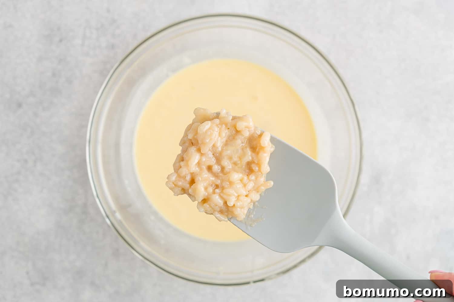 Tempering eggs by slowly adding hot rice mixture to the egg and milk mixture, while whisking.