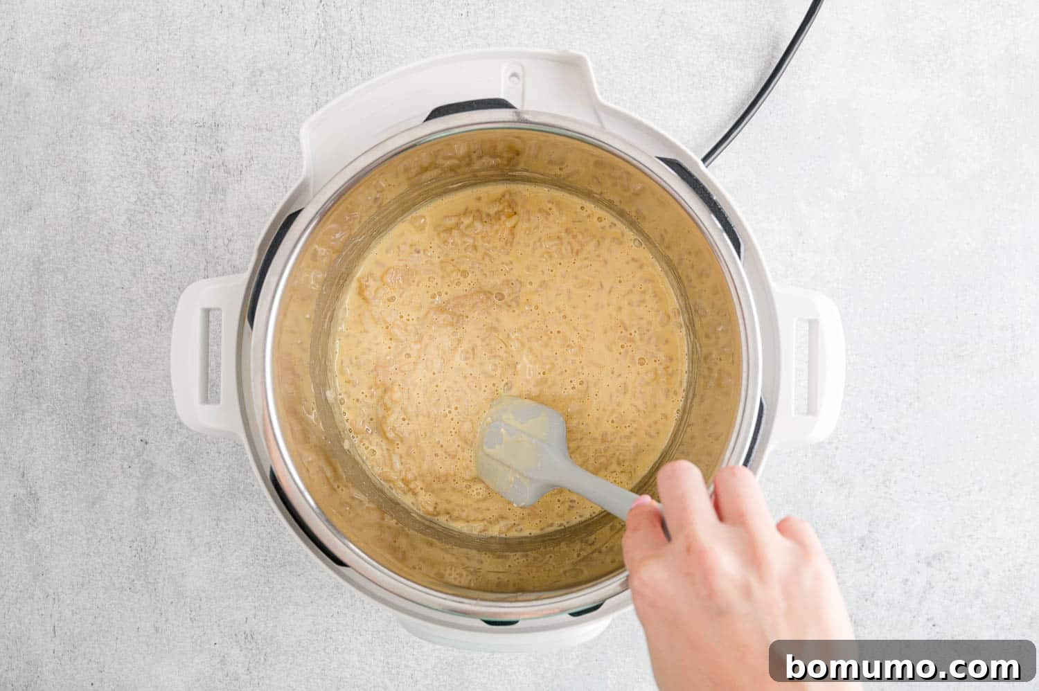 Rice pudding visibly thickening in the Instant Pot on sauté mode, being stirred.