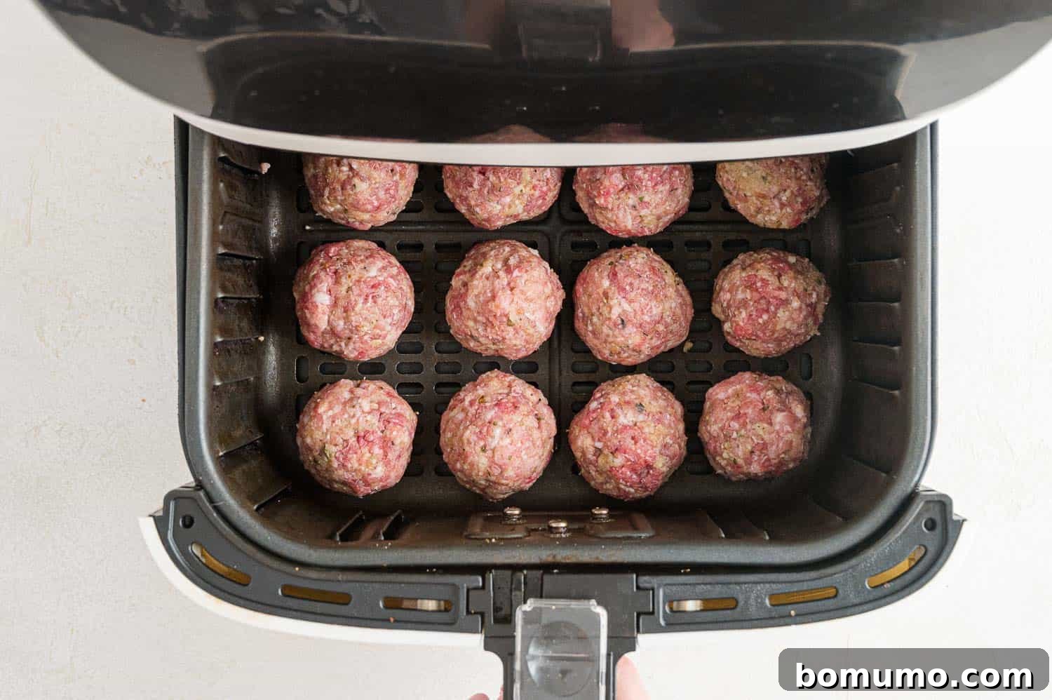 Raw, unbaked meatballs arranged in a single layer inside an air fryer basket.