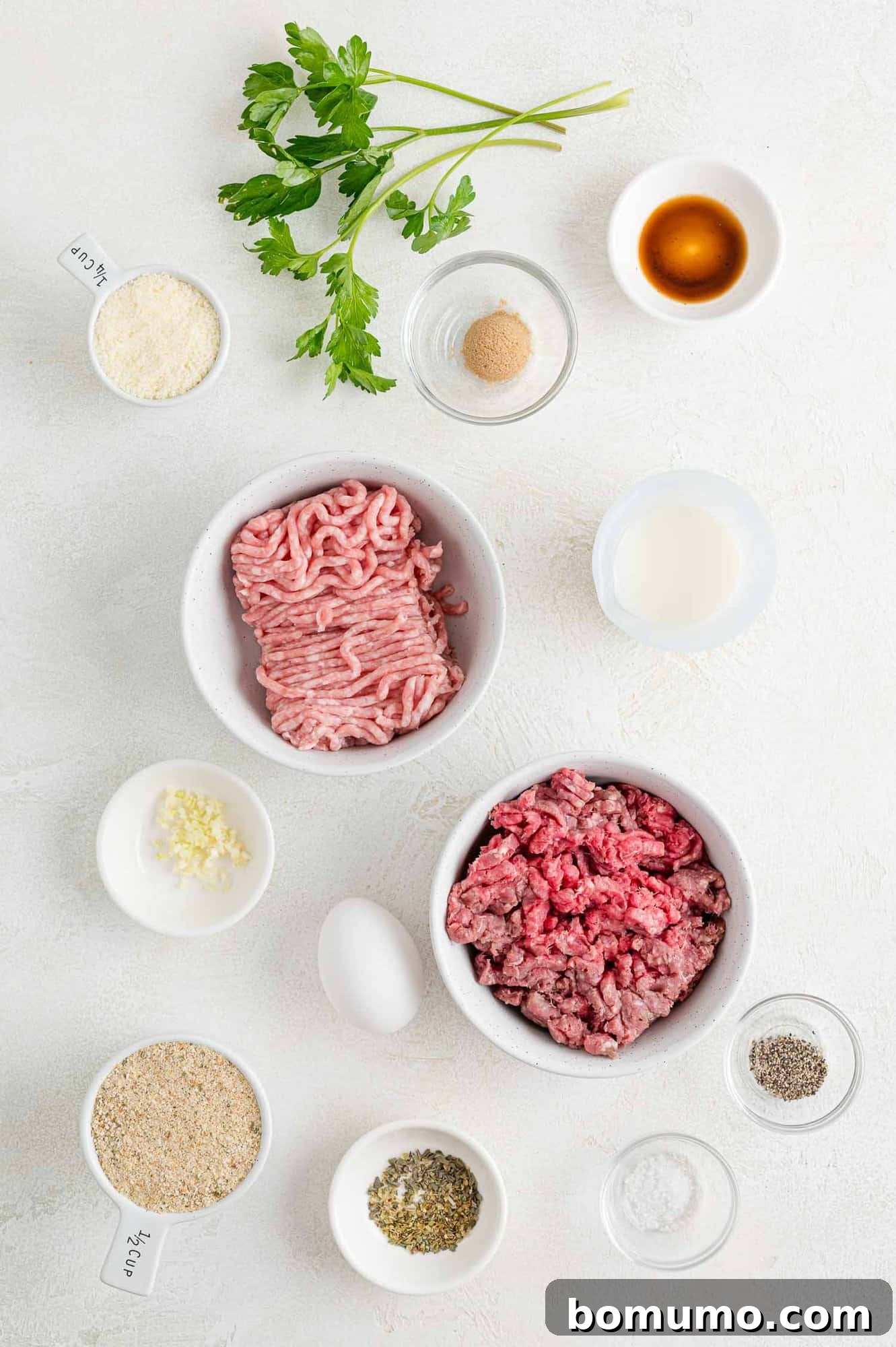 A selection of raw ingredients, including ground pork, ground beef, milk, breadcrumbs, egg, and seasonings, neatly arranged for the recipe.