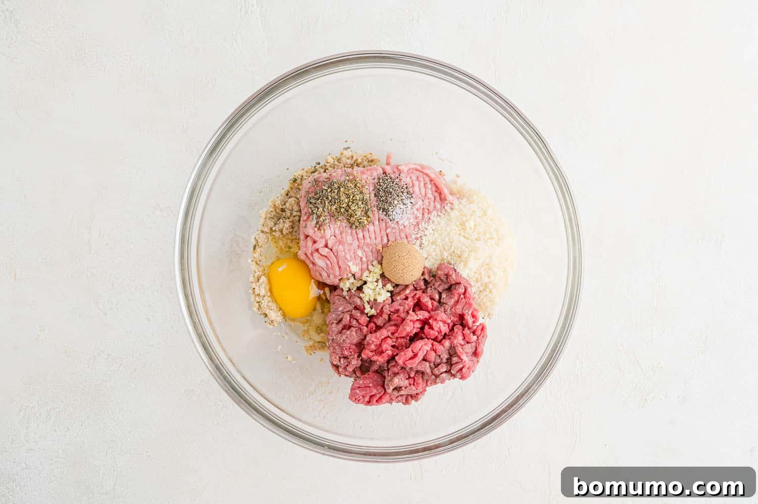 All raw ingredients, including ground meats, egg, cheese, and seasonings, added to the mixing bowl.