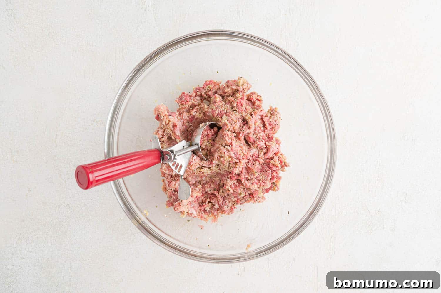 A kitchen scoop filled with meatball mixture, demonstrating the portioning process.