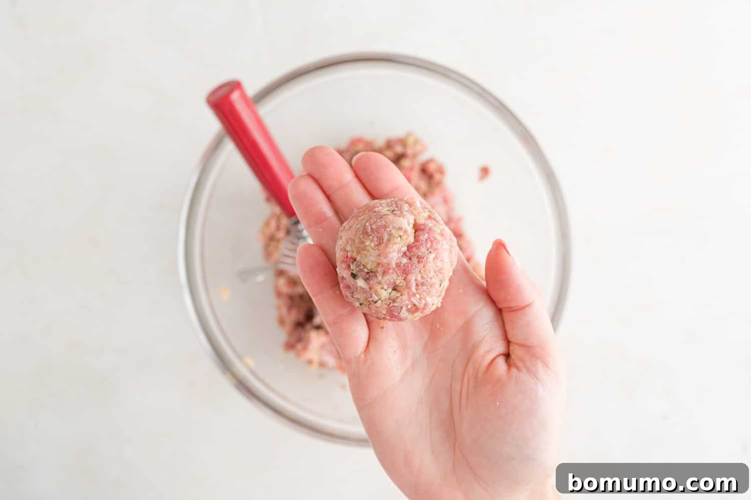 A single, perfectly formed raw meatball, ready for cooking.