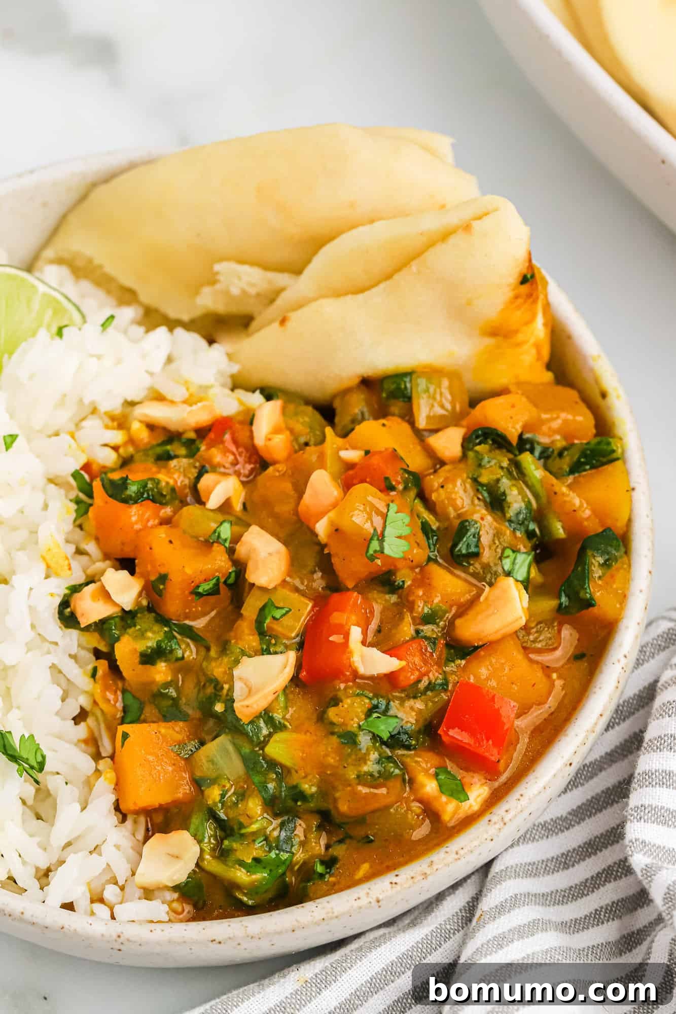 A vibrant bowl of creamy butternut squash curry served with fragrant jasmine rice and a side of warm naan bread, garnished with fresh cilantro.