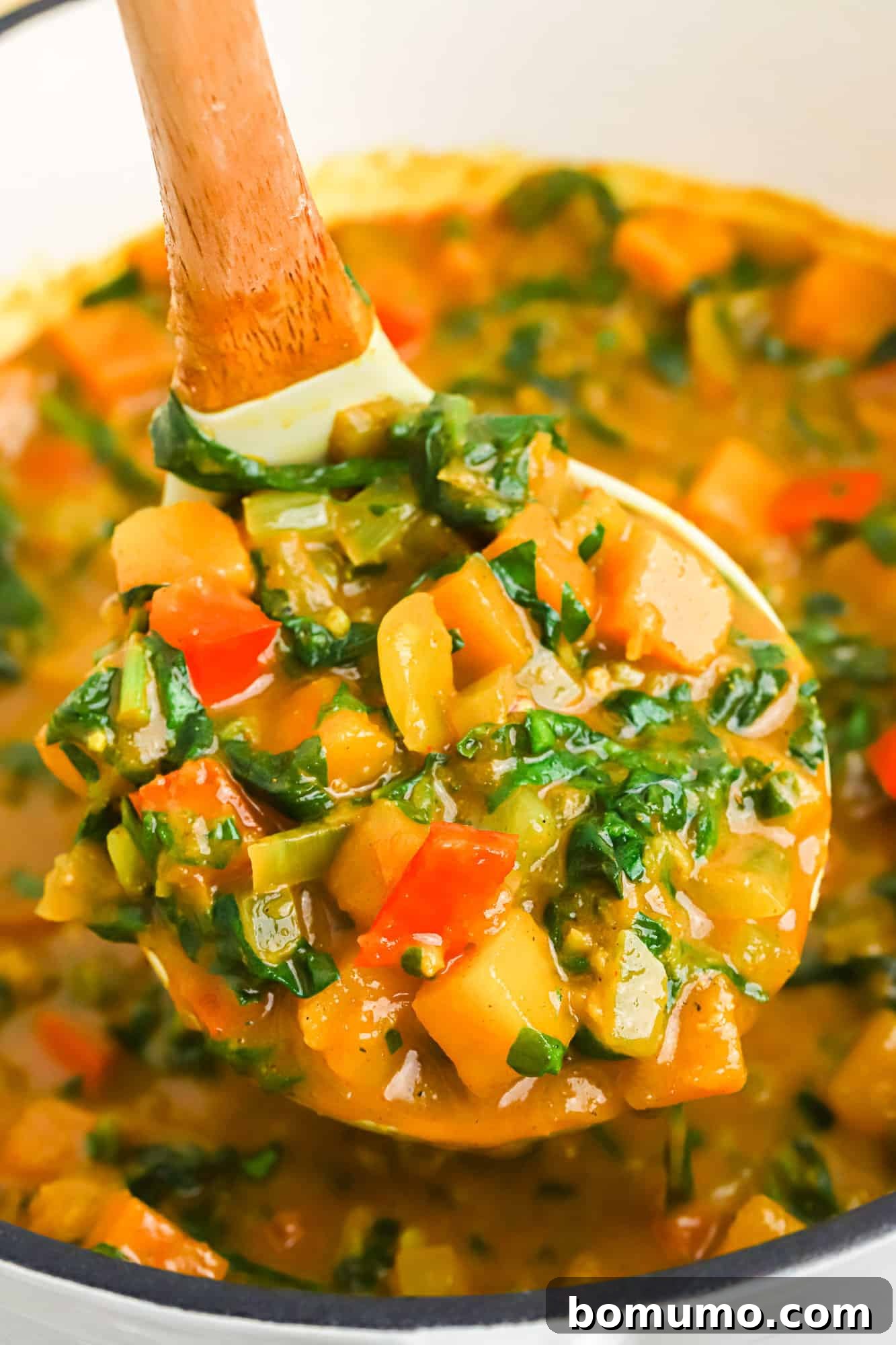A ladle full of rich, creamy butternut squash curry, showcasing the tender squash pieces and vibrant sauce, lifted from a large pot.