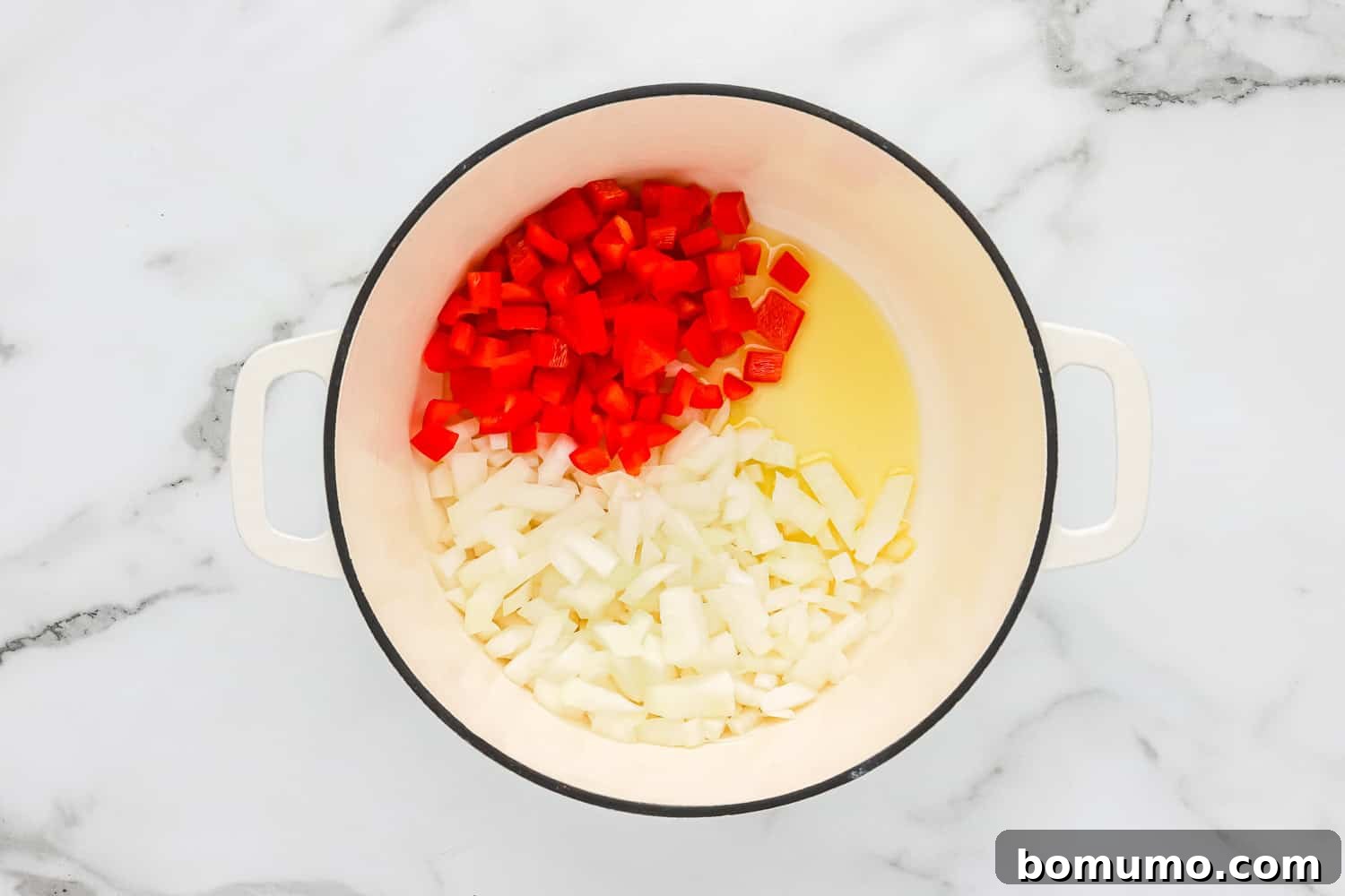 Chopped onions and red bell peppers being sautéed in olive oil in a large Dutch oven, turning translucent and softening.