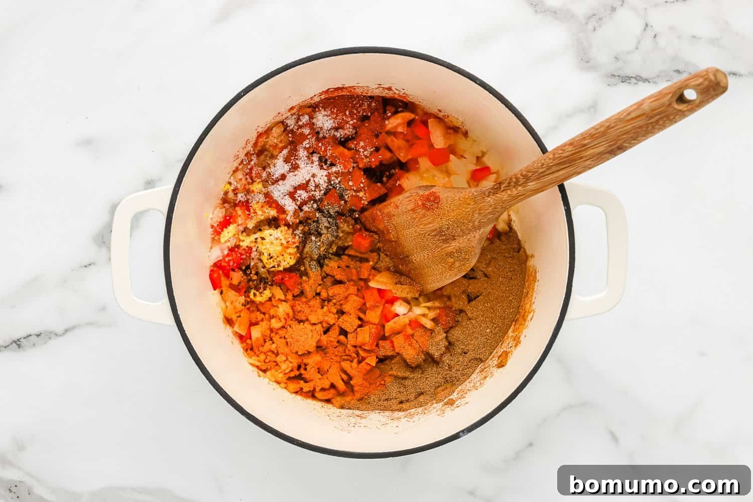The vibrant spice blend, including turmeric and paprika, freshly added to the sautéed onions and bell peppers in the pan, creating a rich base for the curry.