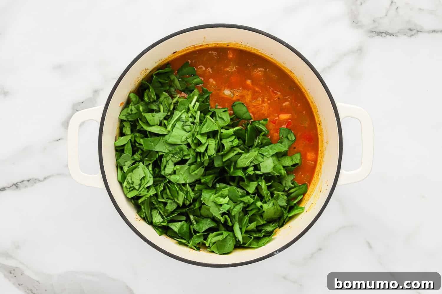 A large pile of fresh baby spinach being added to the hot butternut squash curry in a pot, ready to wilt into the vibrant sauce.