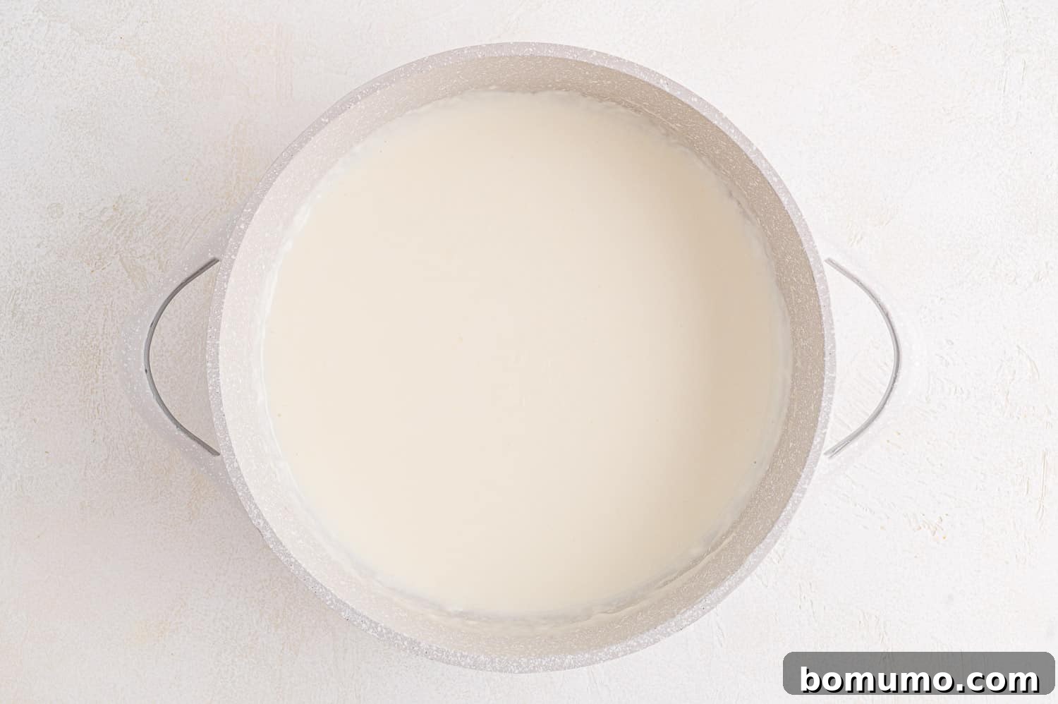 Smooth white sauce cooking in a small pan, thickening.