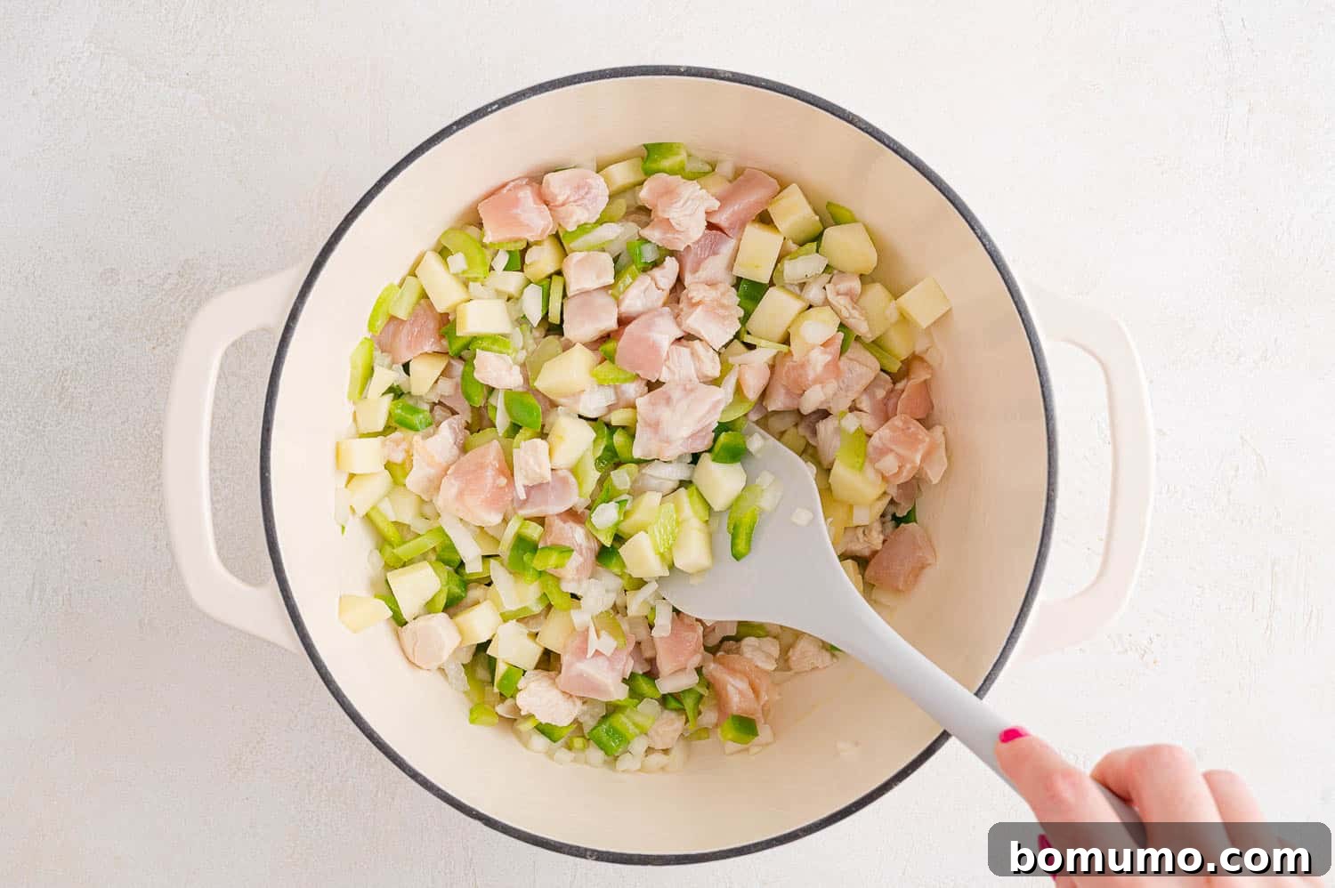 Vegetables and chicken cooking together in a pan, looking softened.
