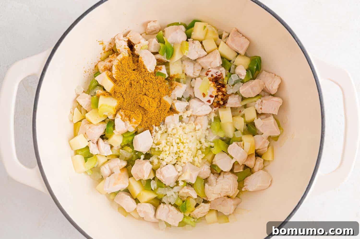 Curry powder being added to the pan with chicken and vegetables.