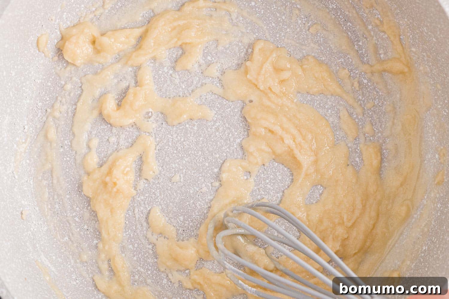 Butter and flour being whisked in a small saucepan to make a roux.