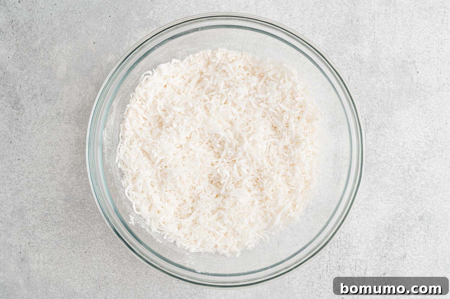Chewy Coconut Delights 6 Flaked coconut thoroughly mixed with flour and sugar in a bowl, forming the dry base for macaroons.