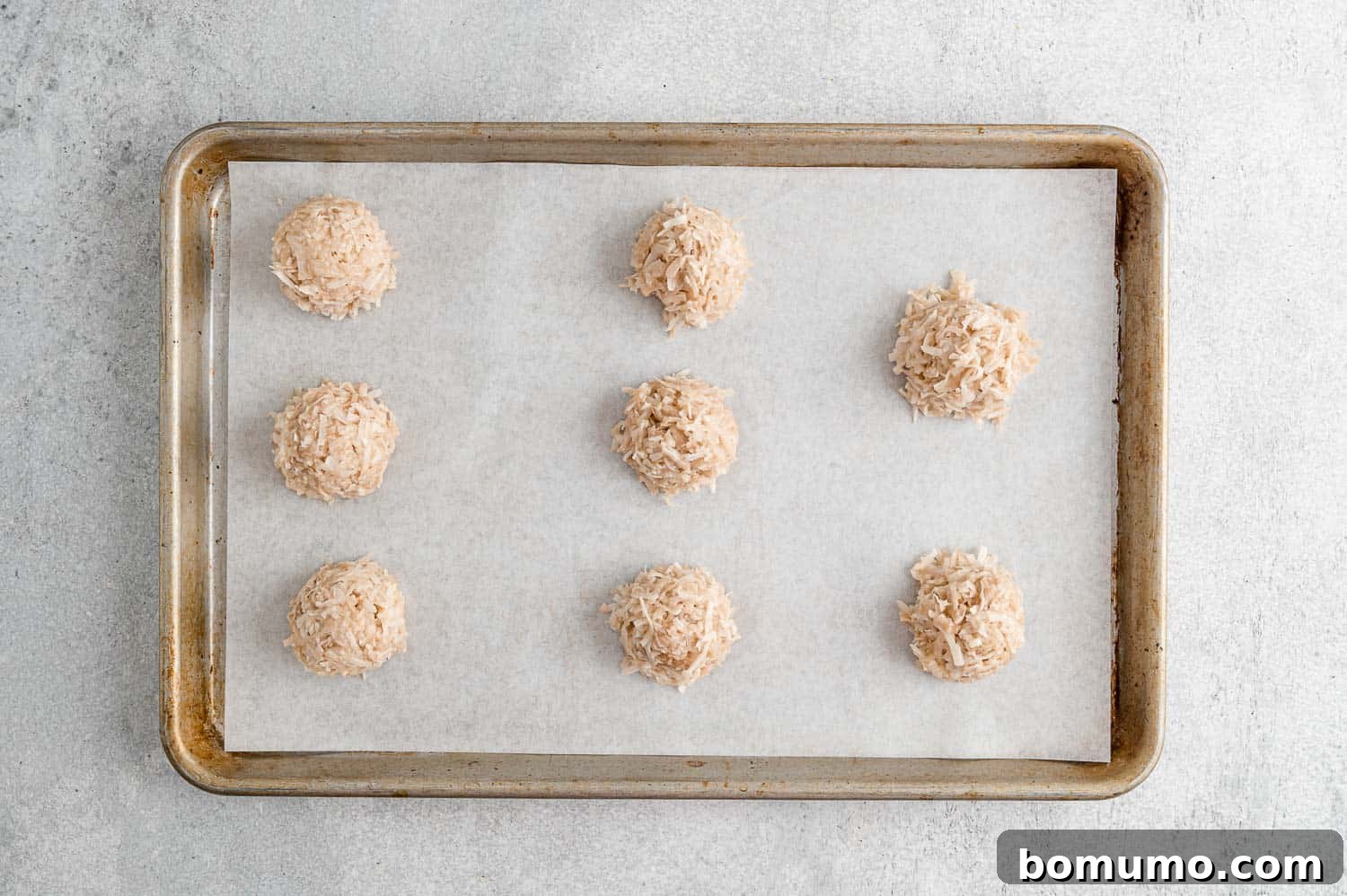 Chewy Coconut Delights 8 Rows of unbaked coconut macaroons, perfectly scooped and shaped, arranged on a parchment-lined baking sheet.