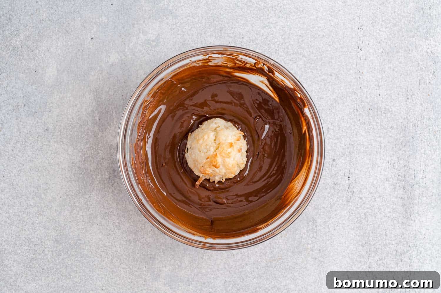 Chewy Coconut Delights 10 A freshly baked coconut macaroon being carefully dipped into a bowl of melted chocolate, creating a decadent coating.