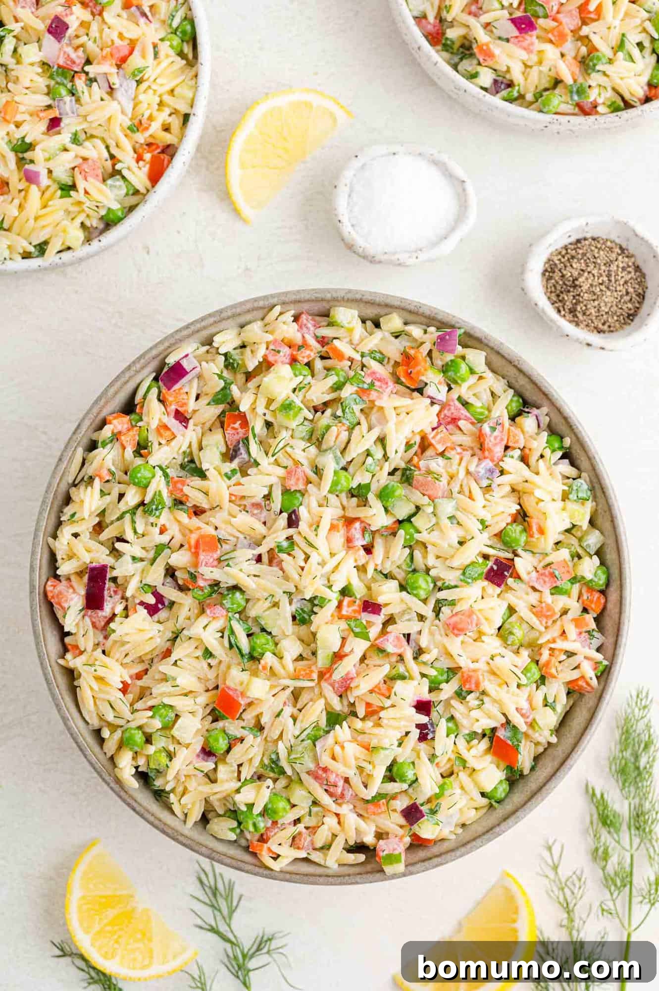 The finished orzo salad, beautifully mixed in a large serving bowl, surrounded by a few key fresh ingredients.