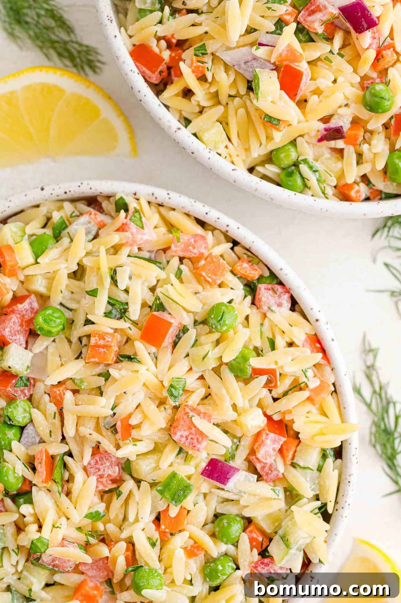 Two bowls of orzo salad with yogurt dressing, showcasing peas, red onions, and tomatoes, ready for serving.