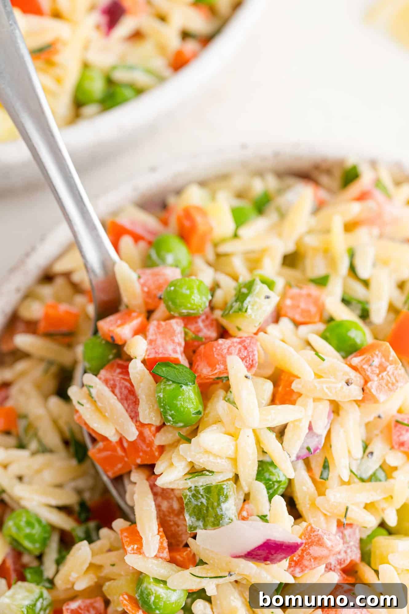 A close-up view of orzo salad with creamy dill dressing served on a spoon, highlighting the pasta and chopped vegetables.