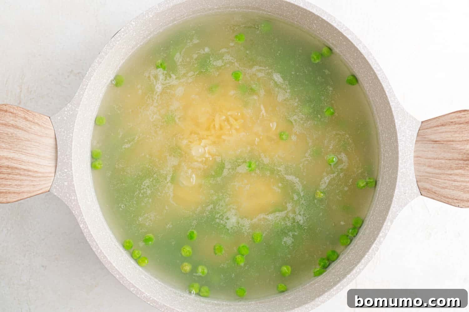Frozen peas being added to the boiling orzo pasta in the pot.