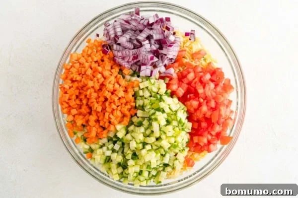 All the cooked orzo, peas, and fresh vegetables are in a large mixing bowl, awaiting the dressing.