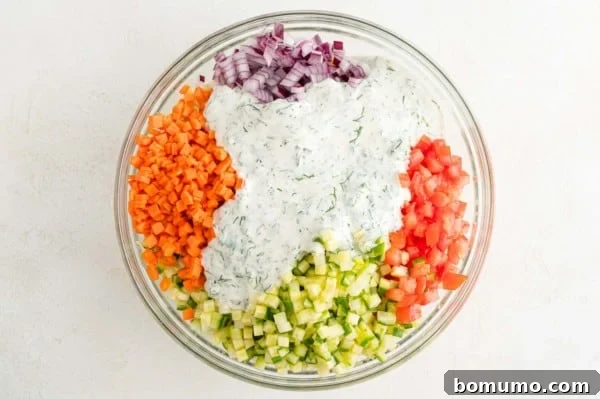 The creamy yogurt dill dressing has just been poured over the orzo and vegetable mixture in the bowl, ready to be tossed.