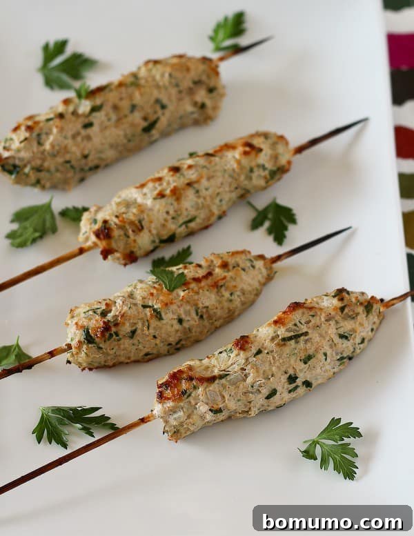 Older photo of four prepared chicken kofta on a white plate, garnished with fresh parsley leaves.
