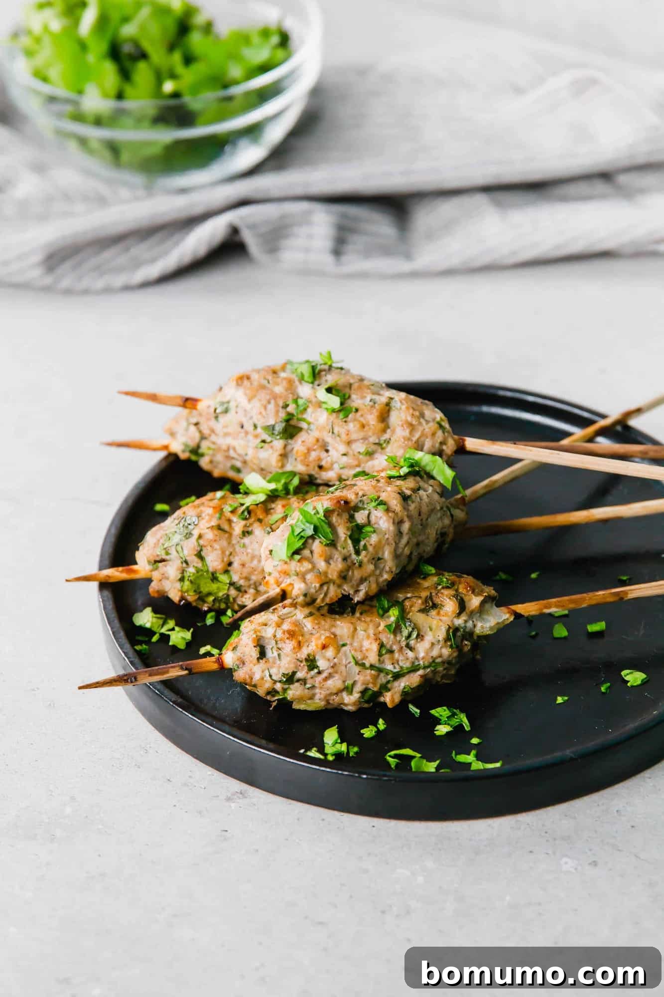 Close-up of several beautifully cooked chicken kofta skewers presented on a small black plate, elegantly garnished with freshly chopped parsley.