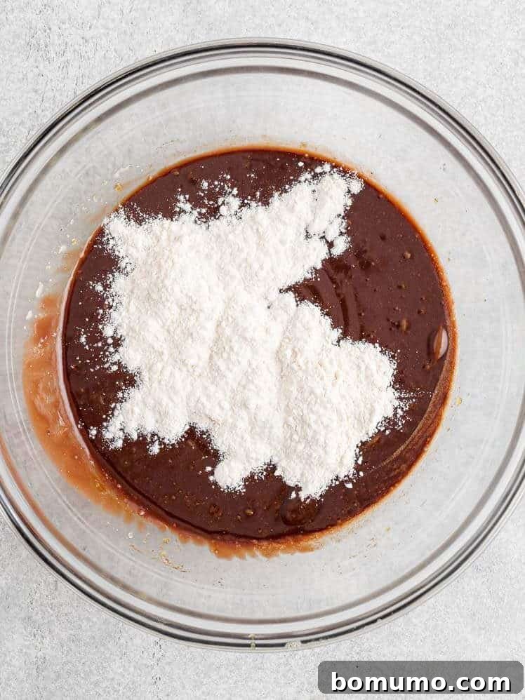 A glass bowl containing chocolate batter with a mound of white flour on top, ready to be mixed.