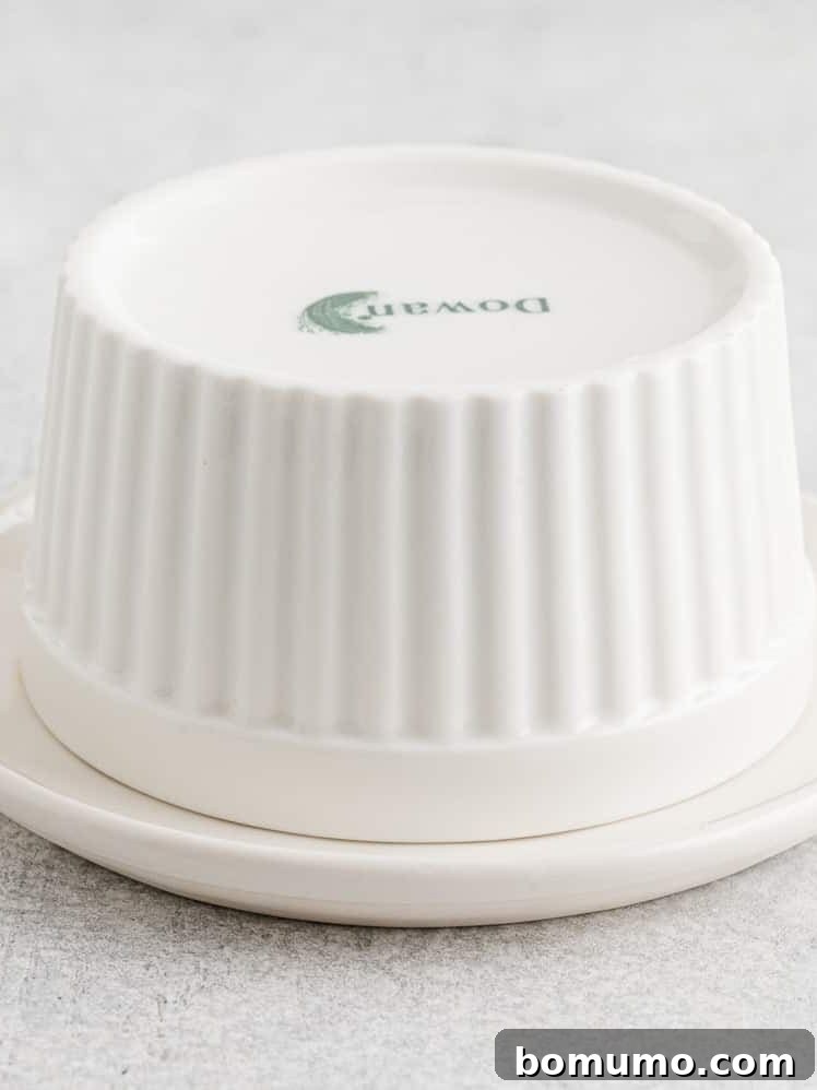 An upside-down white ceramic ramekin sits on a matching saucer, showing a green logo on its base.
