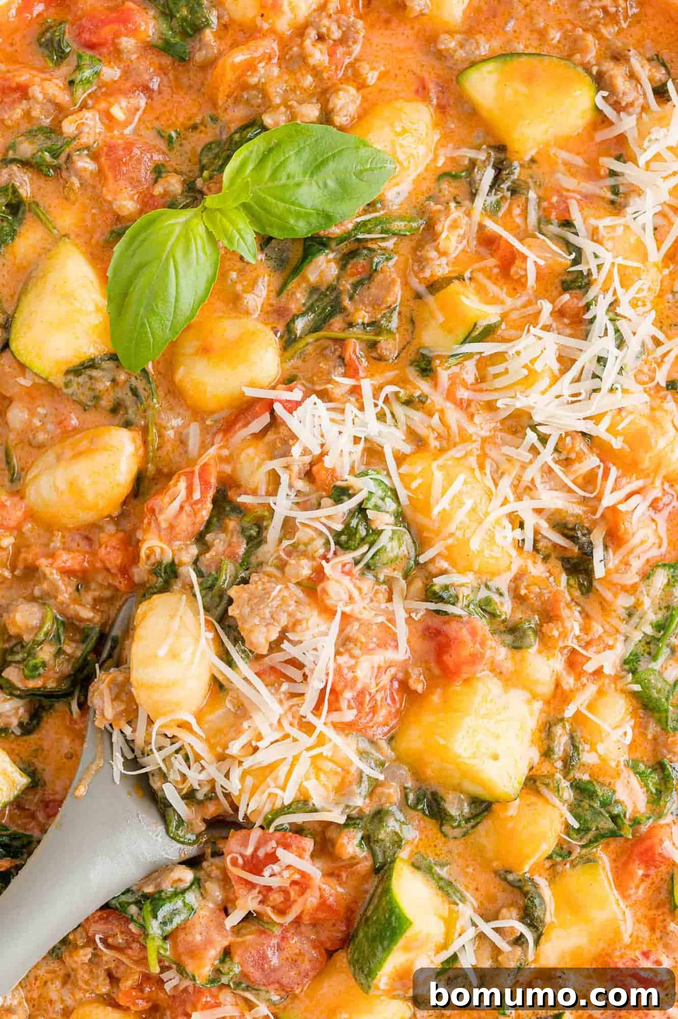 A steaming bowl of creamy one-pan gnocchi with sausage and zucchini, garnished with fresh basil and grated Parmesan.