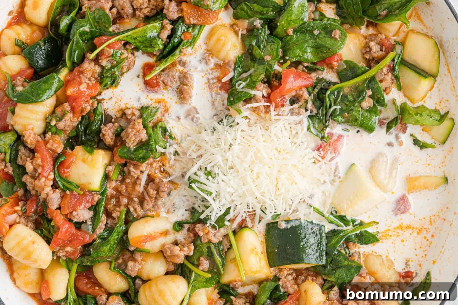 Heavy cream and shredded Parmesan cheese added to the gnocchi and sauce in the pan, making it creamy.