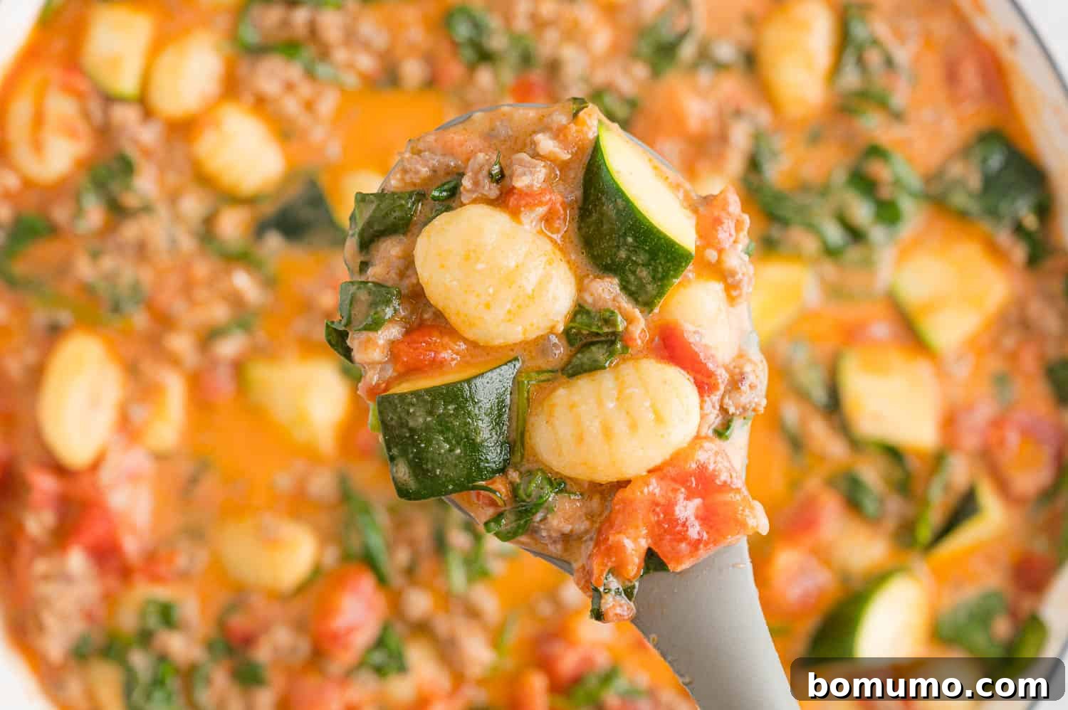 A serving spoon holding a portion of the creamy gnocchi mixture, ready to be served.