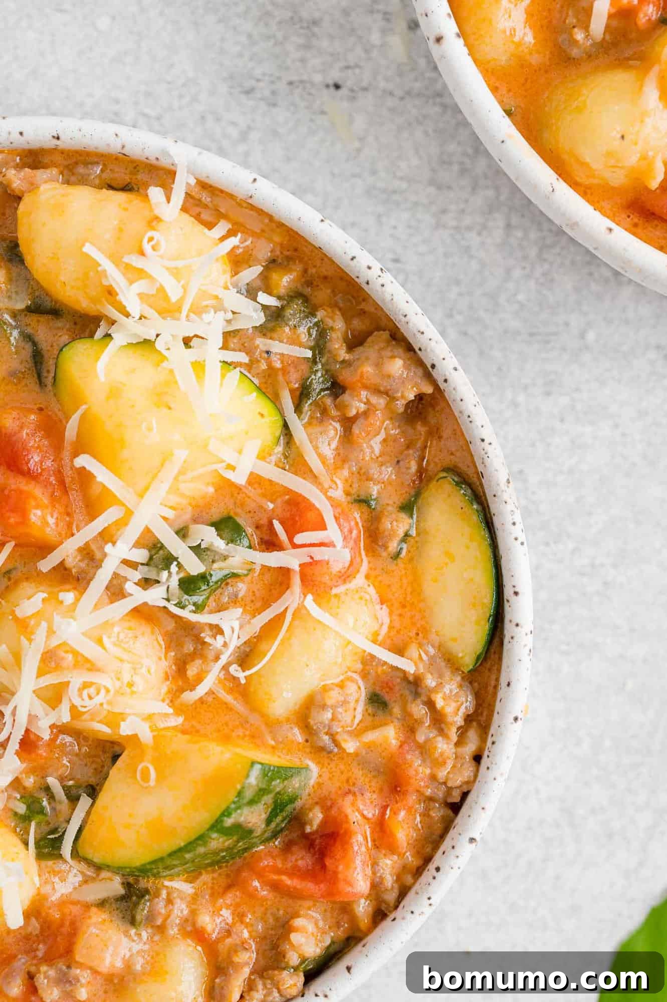 Partial view of a bowl of creamy gnocchi with sausage and zucchini, showing its rich texture.