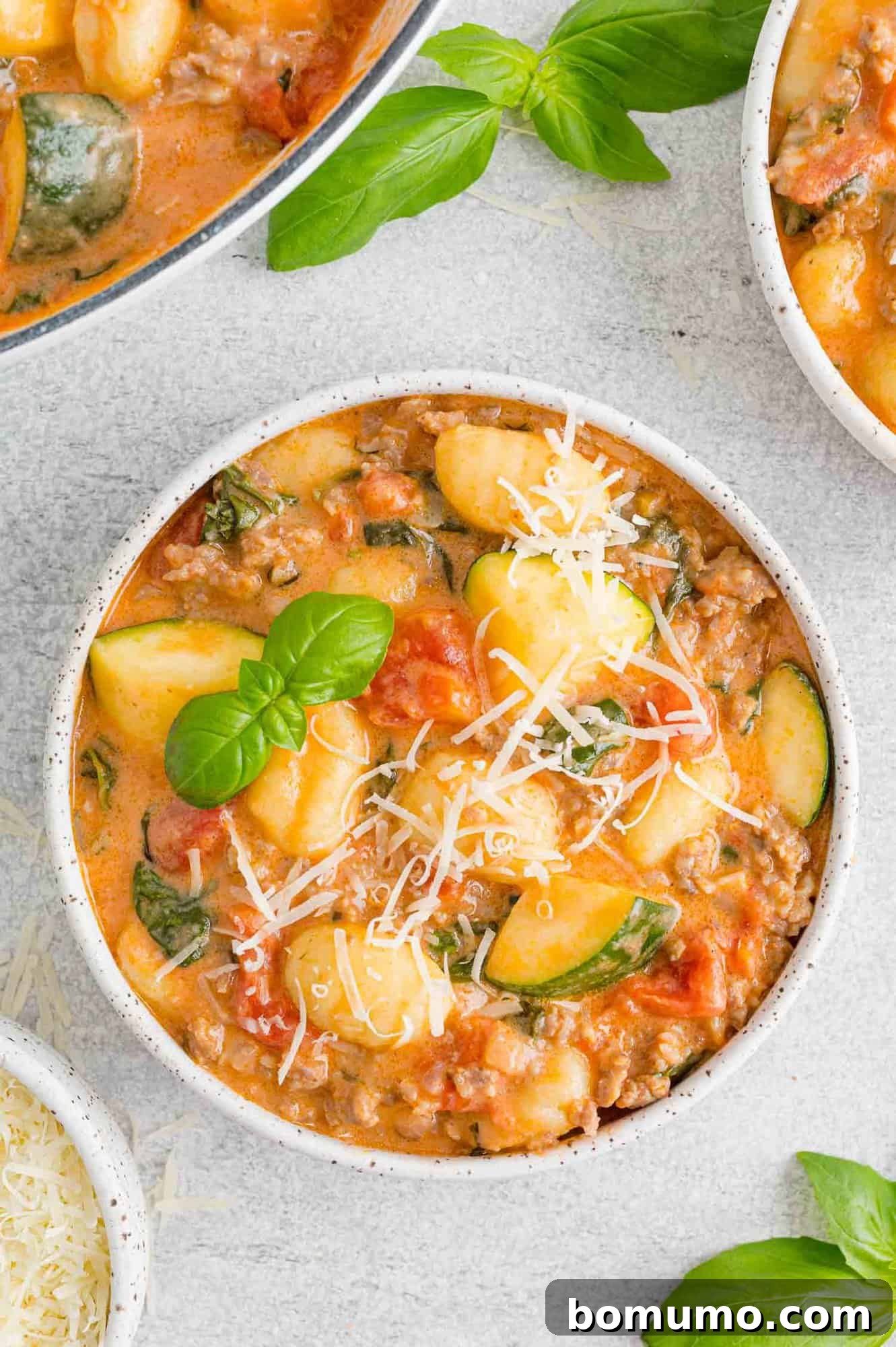 Creamy gnocchi with sausage and zucchini served in a small round bowl, garnished with Parmesan and fresh basil leaves.